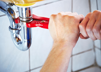 close-up of red wrench held by two hands, tightening sink drain - Plumbing Contractor Messick
