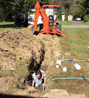 Plumbing Contractor (man) in trench with backhoe visible
